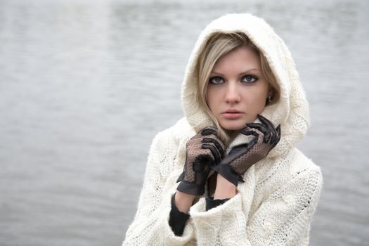 The thoughtful girl in  knitted dress on a background of water
