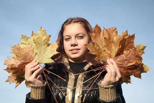 Portrait of  girl with yellow leaves against the blue sky
