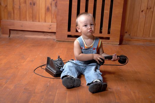 The little boy plays old phone sitting on a floor