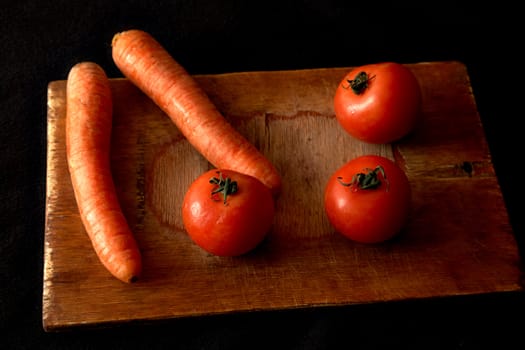 Carrots and tomatoes on an old chopping board a black background