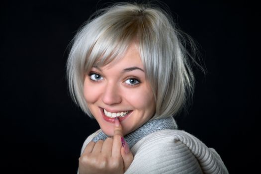 The smiling girl holds a finger at  mouth on  black background