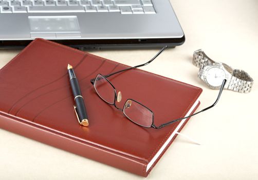 The laptop an organizer a pen and clock on desk