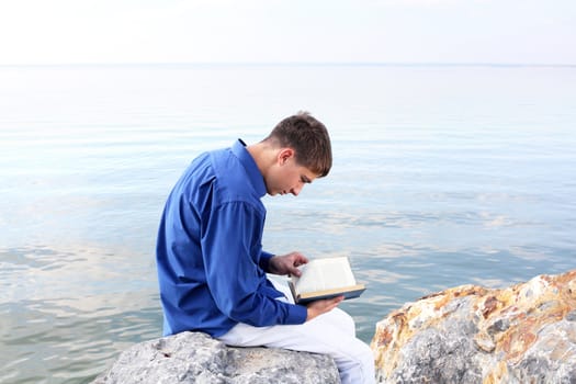 teenager sitting with a book near the water