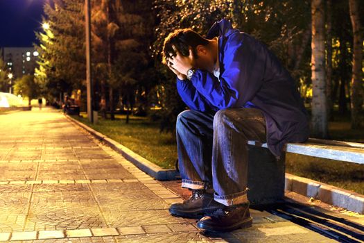 sad and lonely teenager with hidden face sitting in the night park