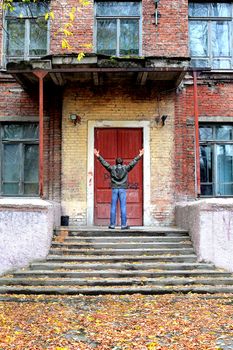 man with hands up in front of the old house with closed door