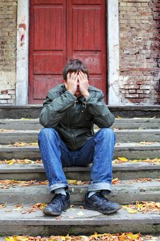 sad young man with hidden face on the old house background