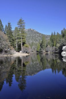 The calm water of Lake Fulmor reflects the surrounding forested landscape on Mount San Jacinto.