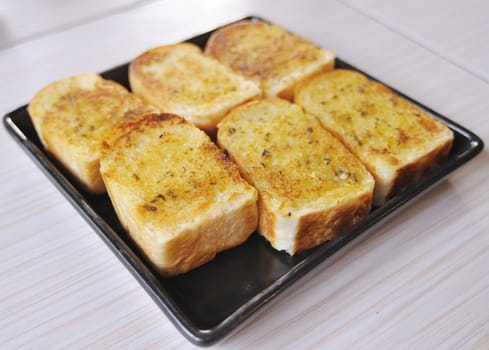 Garlic bread with herbs, on black bread dish.