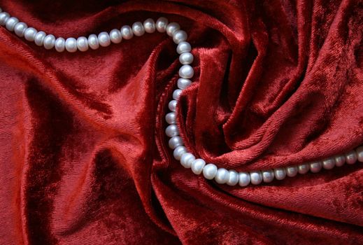 Necklace of white pearls on a terracotta velvet as background 