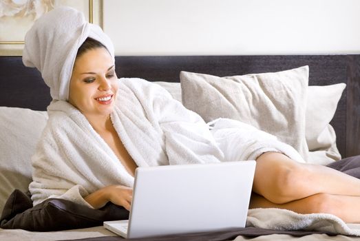 beautiful woman in white bathrobe on a bed with laptop