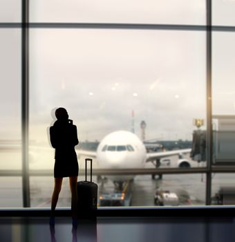 silhouette of businesswoman which expects flight aboard the plane in airport