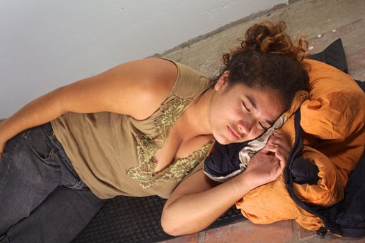 Young Peruvian woman squatting an abandoned house, sleeping on mat and sleeping bag on the floor (Selective Focus, Focus on the face of the woman)