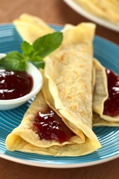 Fresh homemade folded crepes filled with strawberry jam on blue plate (Selective Focus, Focus on the front of the jam on the crepe)