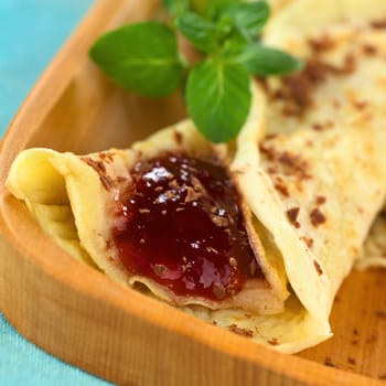 Fresh homemade folded crepe filled with strawberry jam and sprinkled with chocolate pieces on wooden plate (Selective Focus, Focus on the front of the jam)