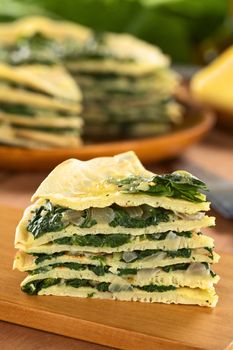 A piece of fresh homemade savory crepes layered with chard (mangold) and onion with cheese on top on wooden board (Selective Focus, Focus on the front of the piece) 