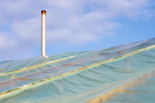 Fragment of film greenhouses with the chimney against the sky