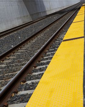 Diminishing straight train tracks at station with yellow boarding area