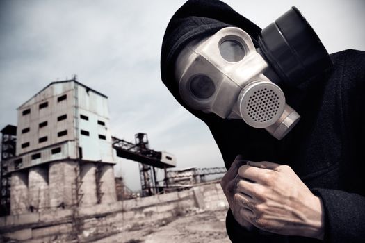Human in gas mask outdoors and industrial factory on a background