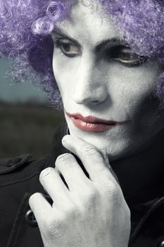 Single sad clown with theatrical makeup and wig. Vertical photo with dramatic colors and toning