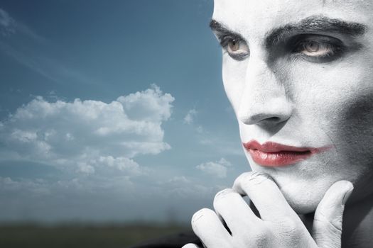 Pensive clown outdoors with theatrical makeup. Horizontal photo, artistic colors and darkness added 