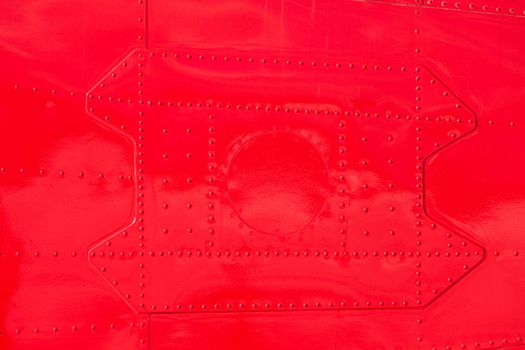 Bright red painted riveted metal sheet skin of airplane fuselage background texture pattern