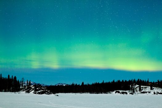 Spectacular display of intense green Northern Lights or Aurora borealis or polar lights over snowy northern winter landscape