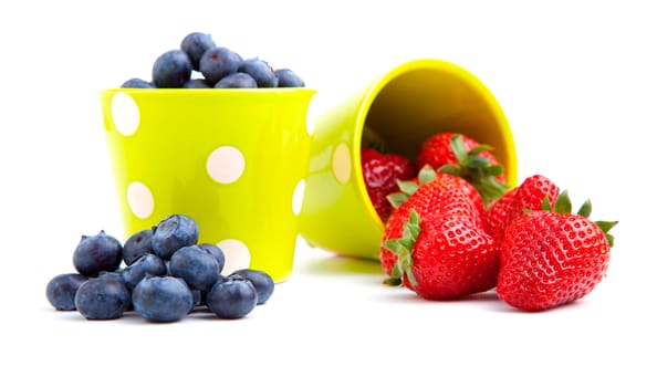 Assorted fresh picked berries in a green mug over a white background. Vertical format with reflection.