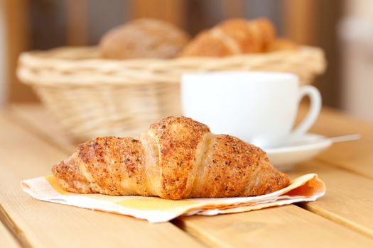 Fresh croissant and white cup coffee, on a wooden table