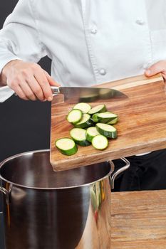 Photo of a chef pushing chopped zucchini into a large cooking pot.