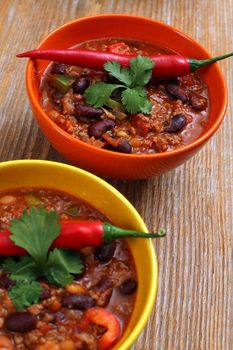 Photo of two bowls of chili resting on an old wood table.