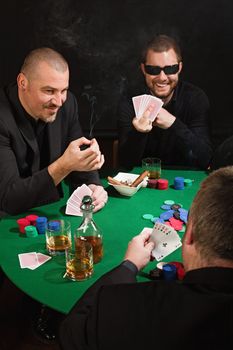 Photo of three men playing poker, smoking cigars, drinking whiskey and one flipping the bird at the player with the good poker hand.