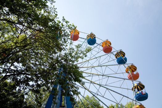 Popular attraction in park - a Ferris wheel on a background of the cloudy blue sky