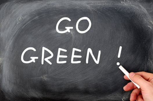 "Go Green" written on a chalkboard background with a hand holding chalk