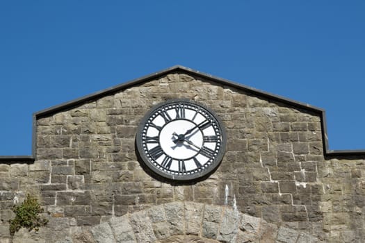 A clock with roman numerals on a stone wall painted black and white with a clear blue sky in the background.