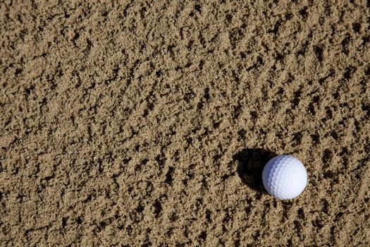 a golfball lying in a sand bunker on a golf course