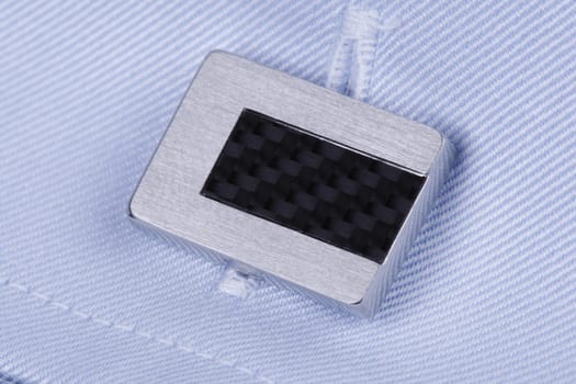 close-up of a silver cuff-link with carbon on a light blue business shirt