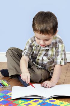 Cute little boy focused while coloring a blank white paper page with a red pen.