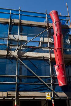 A set of scaffolding with blue safety netting a danger sign and a red rubble shoot.