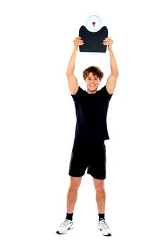 Male athlete standing and showing weighing machine against white background