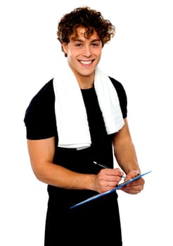 Smiling male trainer writing on clipboard. Towel around his neck