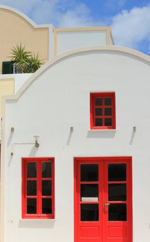 Colorful facade of a house with its red door and windows and yellow and white facade by beautiful weather, Santorini, Greece.