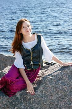 Medieval woman sitting on a big rock near the sea