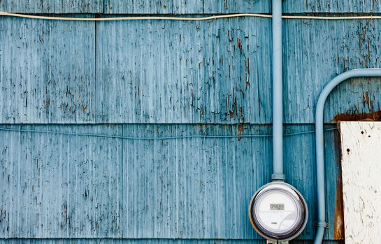 Modern smart grid residential digital power supply meter mounted on grungy blue exterior wooden wall