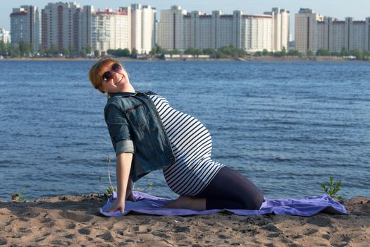 Pregnant woman doing gymnastic exercises on the river coast