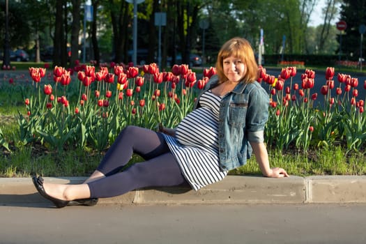 Pregnant woman sitting near tulip flowerbed