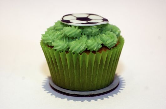 A cupcake with green frosting and a flat sugar 'football' on the stop, against a white background with copy space.