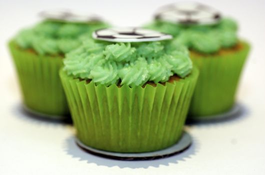 Three cupcakes with green frosting and a flat sugar 'football' on the stop, against a white background with copy space.