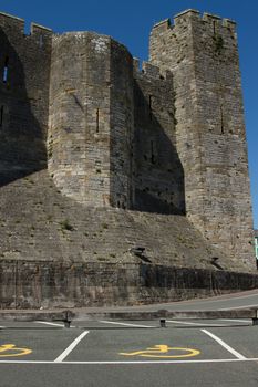 A parking space with a yellow disabled symbol in front of tall castle walls.