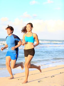 Sport couple running on beach during outdoor fitness exercise.  Asian woman and caucasian man runners.