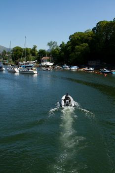 An inflatable boat entering a marina with a following wake and yachts in the distance.